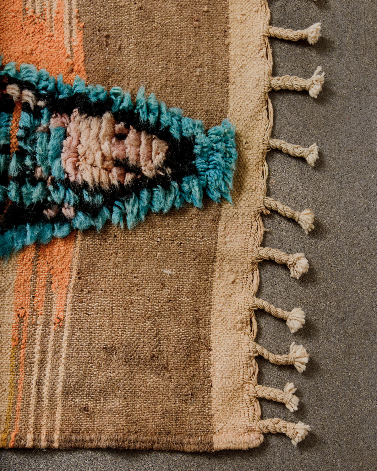 Corner of Berber runner rug with brightly coloured wool pile, flat weave and natural wool tassels.